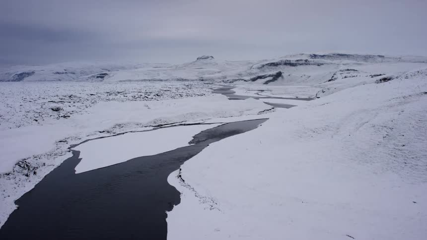 A river flowing through an icy landscape seen in aerial view