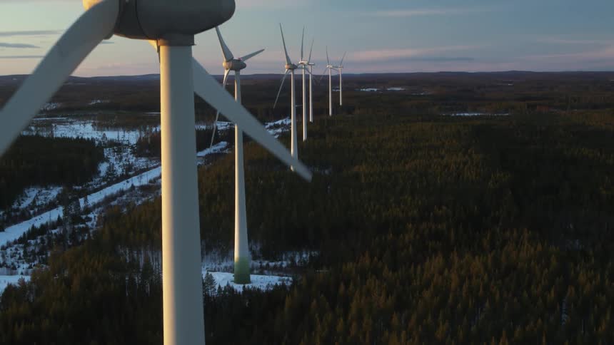 A row of wind turbines are being filmed from a drone