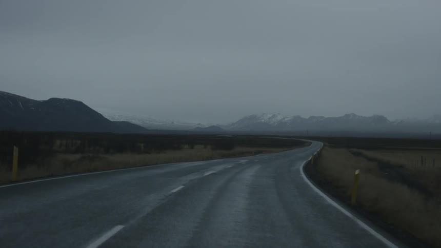 Driving along a damp asphalt road between mountain ranges