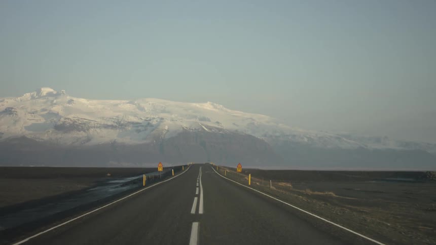 View down a long straight road with a snow capped mountain in the distance