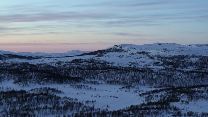 Snow and pine trees cover a mountain landscape at sunset