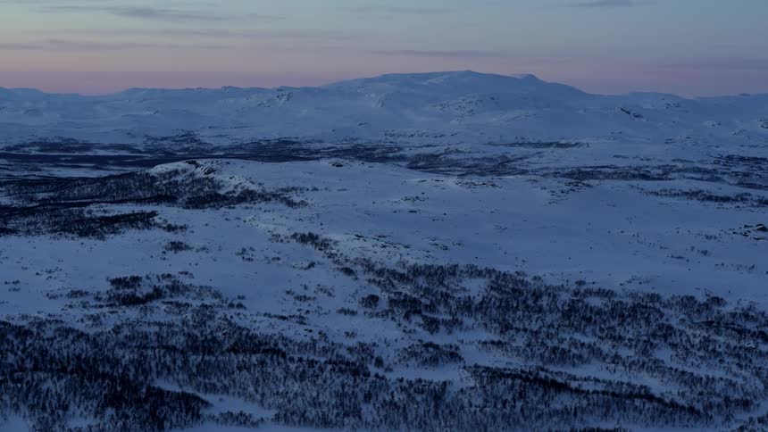 A cold and snowy landscape is filmed from a drone at dusk