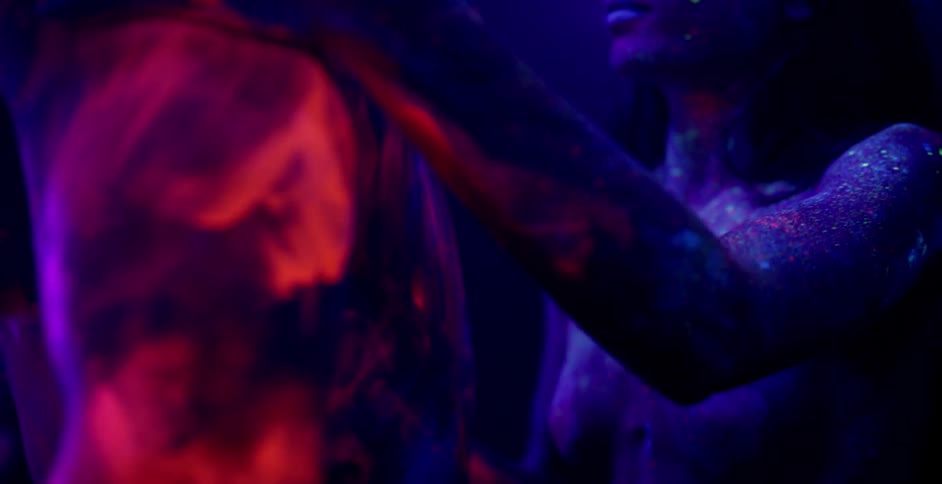 A man and woman in glowing body paint touch