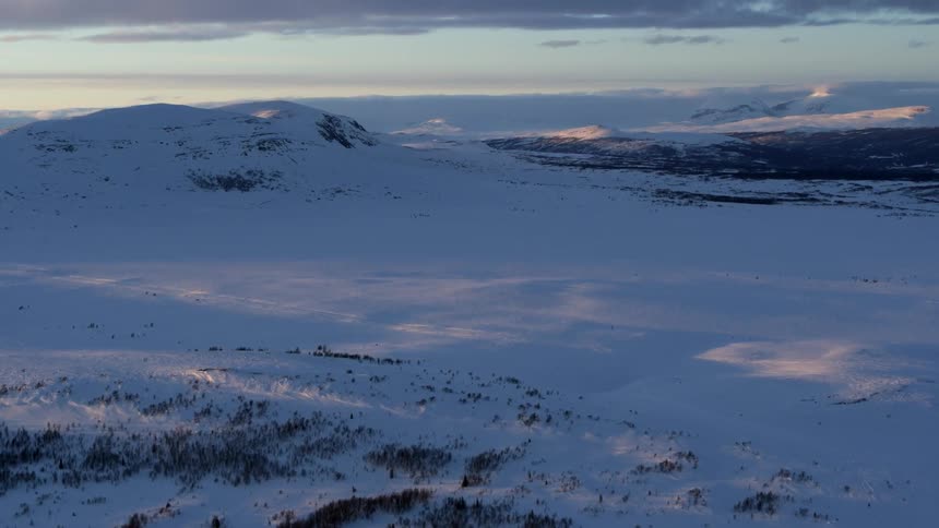 Snow covers a mountain landscape at sunset