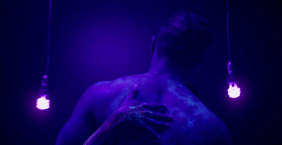 A man without a shirt is embracing a woman in a dimly lit purple room