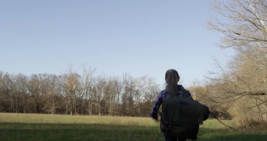 A young girl runs outside in a field carrying a bag