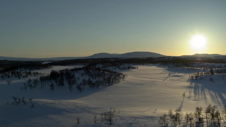 The sun sets over snow covered fields and trees