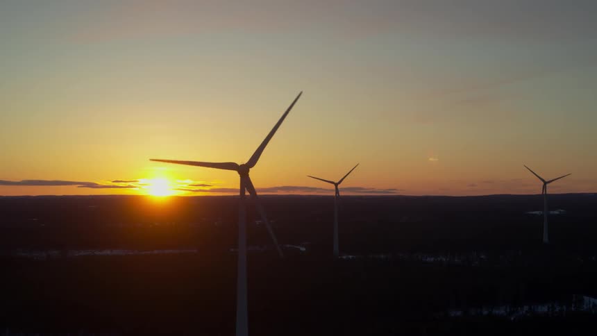 Wind turbines are spinning with the sun on the horizon