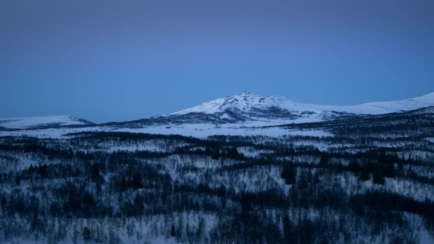 A snow covered mountain and valley is being filmed by a drone