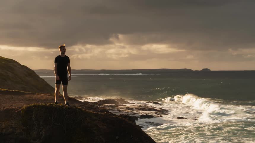 A man walks slowly to the cliff to look out over the water
