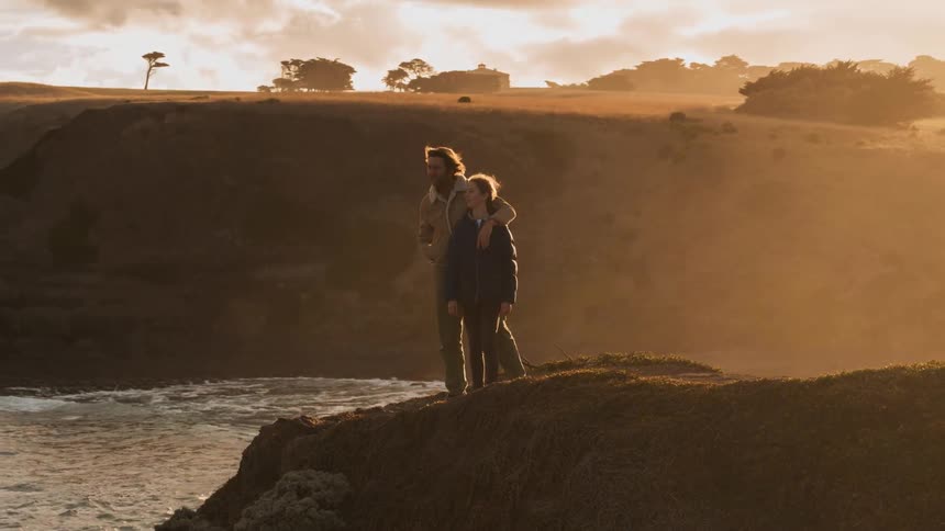 Two people sit by the edge lookout out over the water