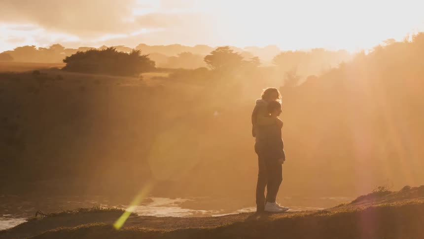 Two people hug and look out from atop a mountain