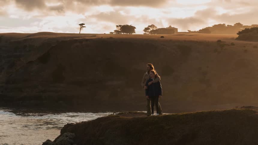 Man hugs child standing at the edge of a cliff overlooking water