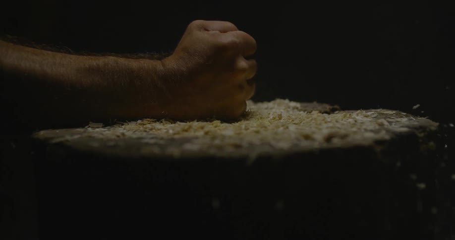 A man bangs his hand down on some wood shavings