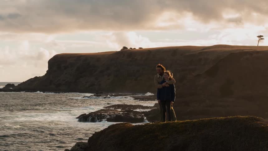 Two people hug on the cliff near the shore