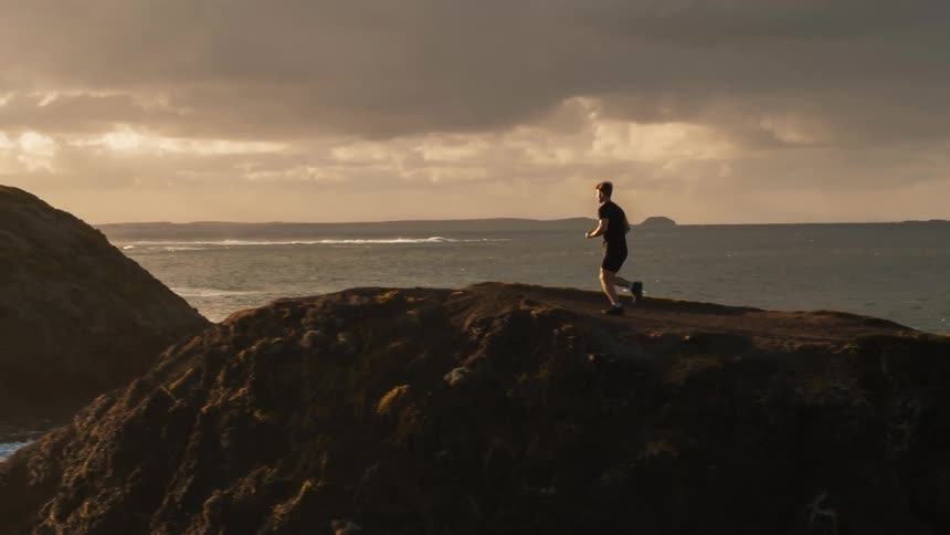 A man jogs along the coast at sunset