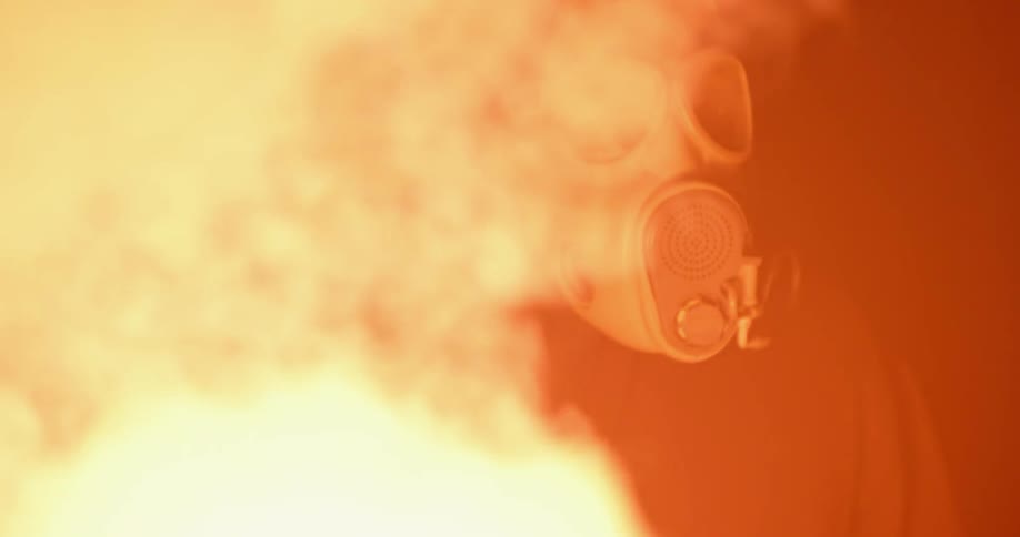 A man wearing a gas mask holds a lit flare