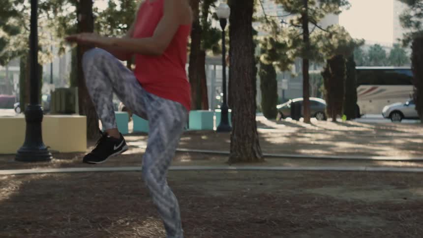 A woman jogs and does knee lifts outdoors