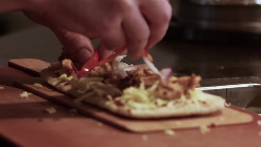 Red peppers are sprinkled onto a pizza