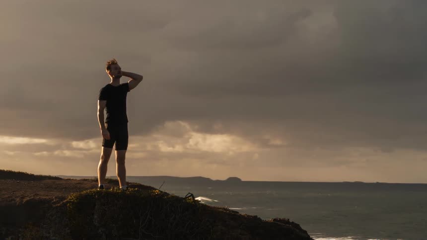 A man is standing on top of a cliff next to the ocean