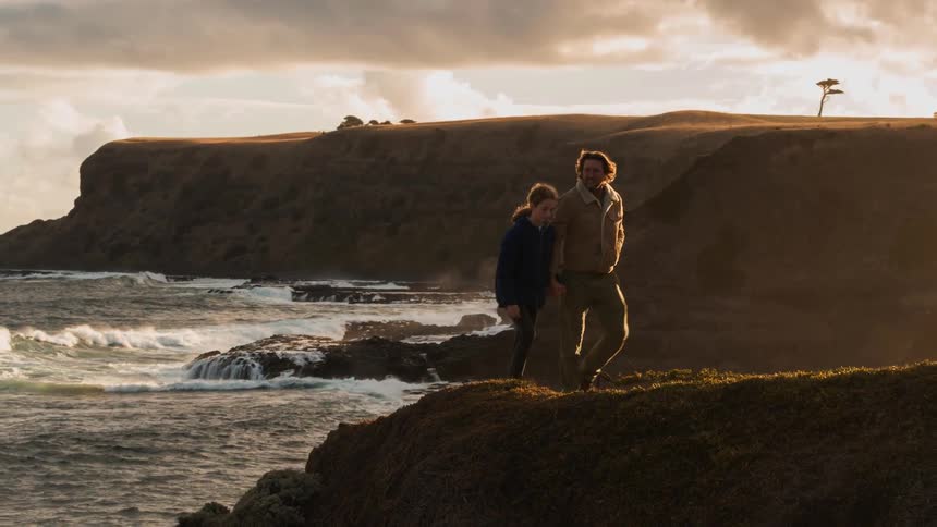 Man hugs child standing at the edge of a cliff overlooking water