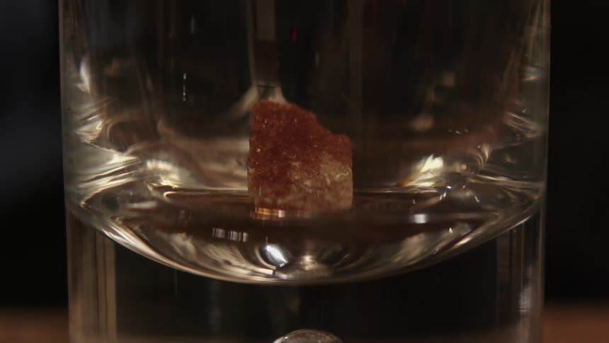 Liquor is poured into a glass with a block of brown sugar in it