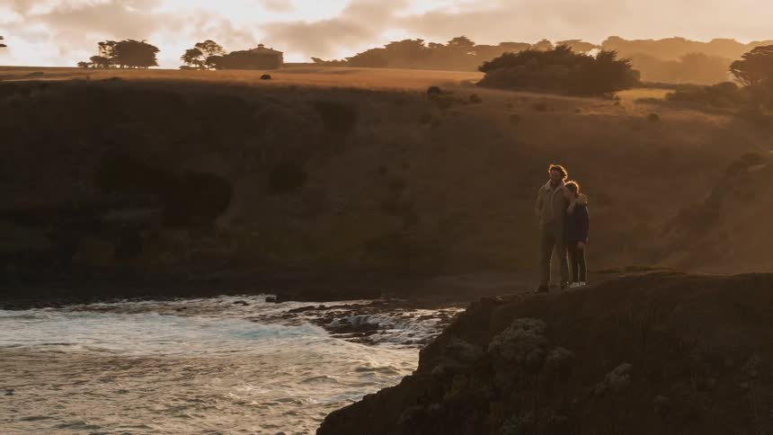 A man and girl walk out to a coastal cliff's edge to take in a view