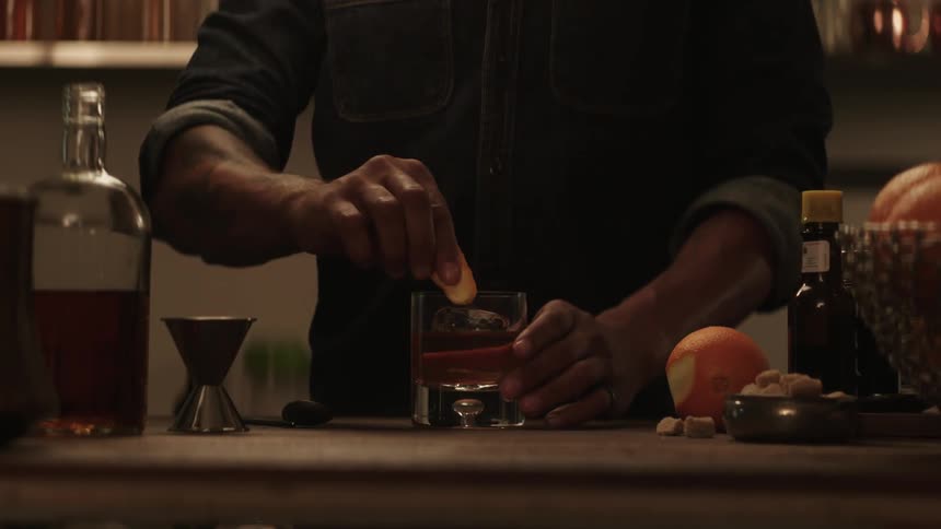 Man peels an orange then rubs the rind around the rim of a glass