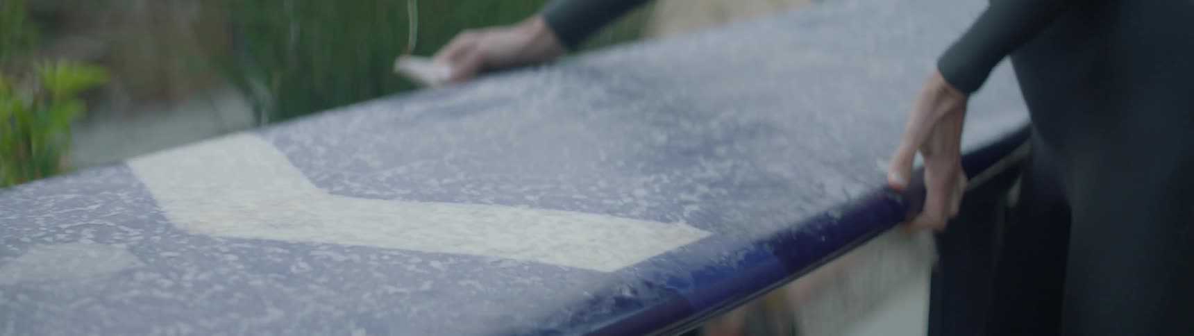 A surfer picks up a surfboard and waxes the bottom