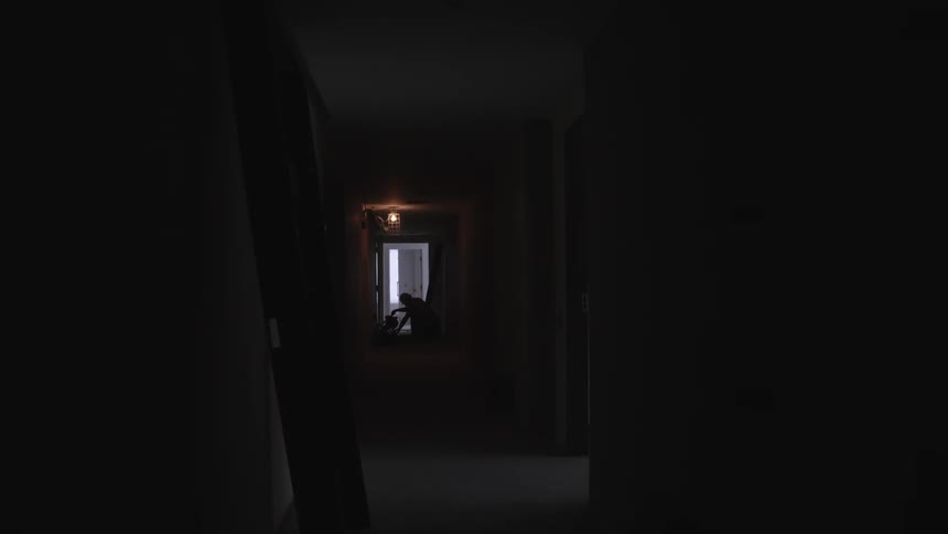 A person stands at the end of a dark hallway