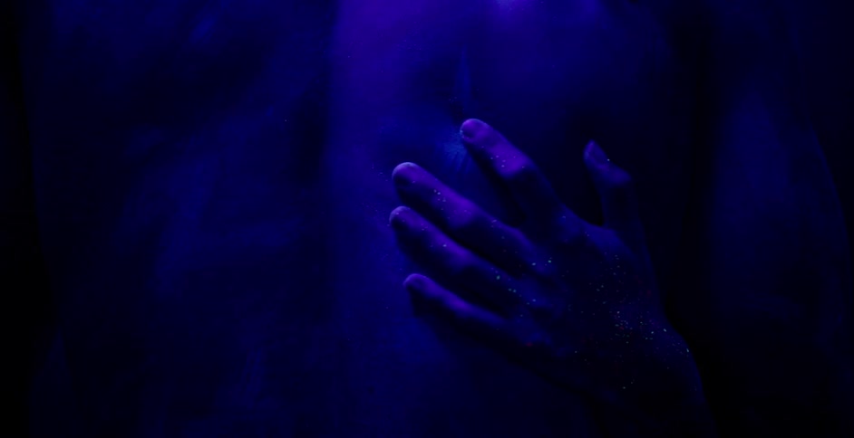 A woman grasps at a man's back in the dark
