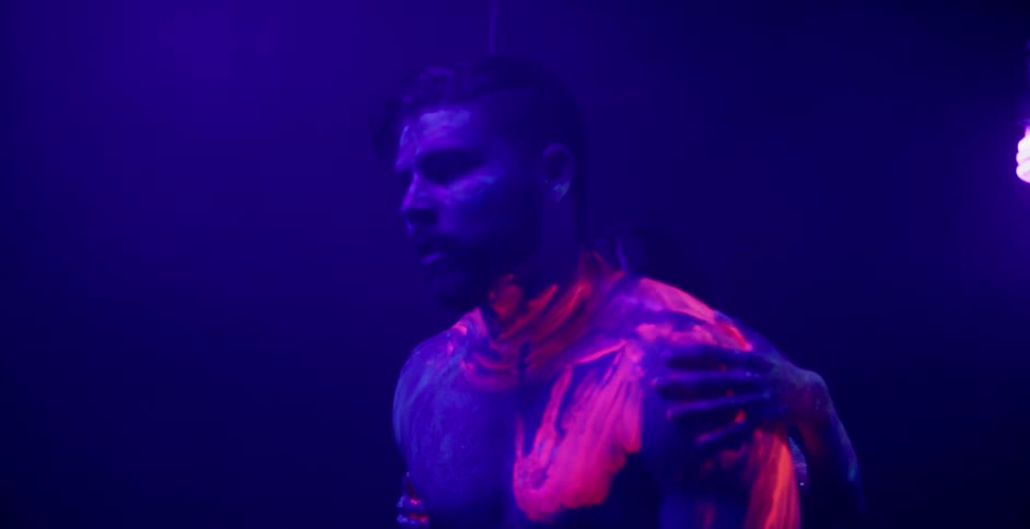 A woman rubs glowing paint onto a man's body