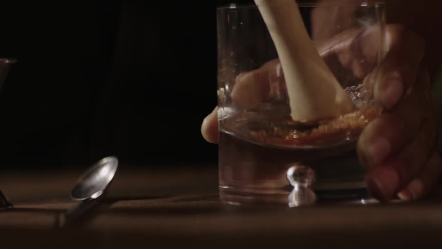 A bartender is muddling a sugar cube in a glass