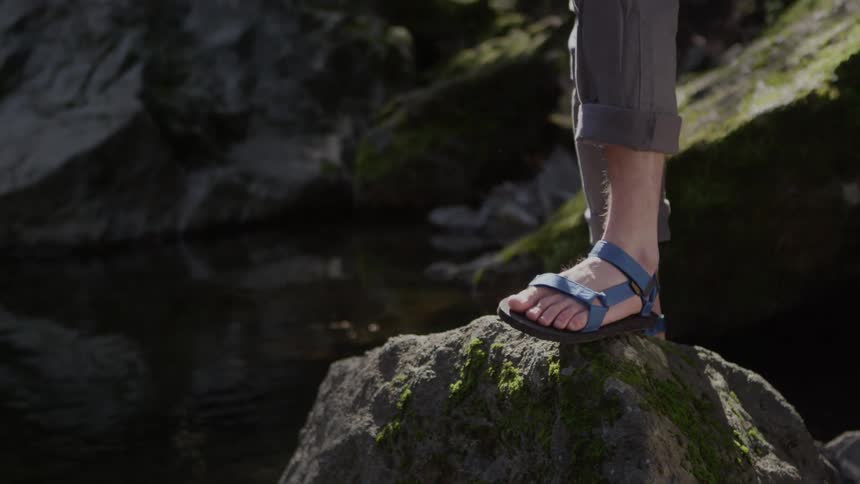 A person in sandals walks over large rocks