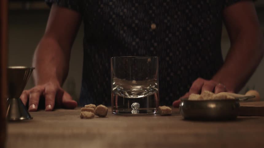 A man stands at a bar in front of various ingredients for a cocktail