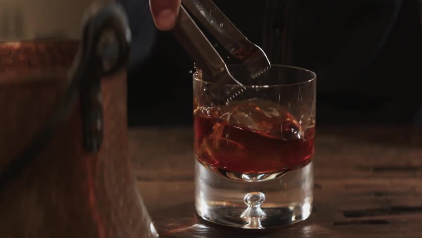 Person uses small tongs to put a piece of ice into a drink