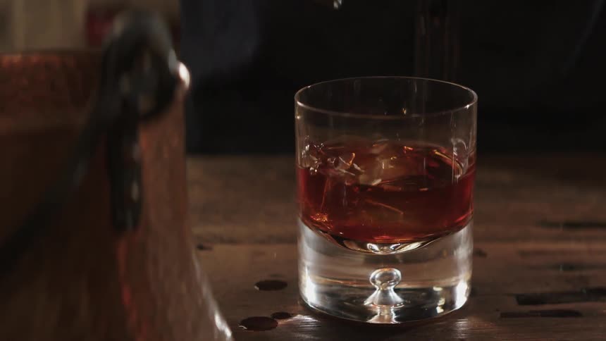 Ice cube is picked up with tongs and dropped into a beverage glass