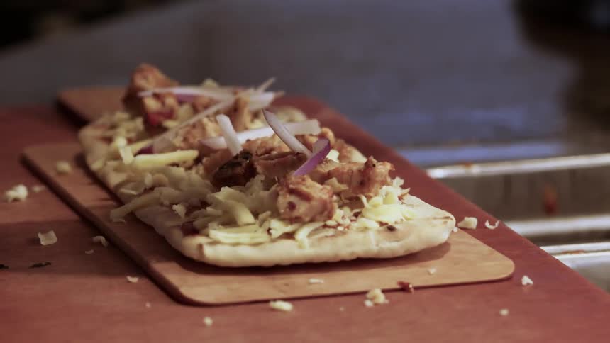 A person is putting ingredients on a pizza