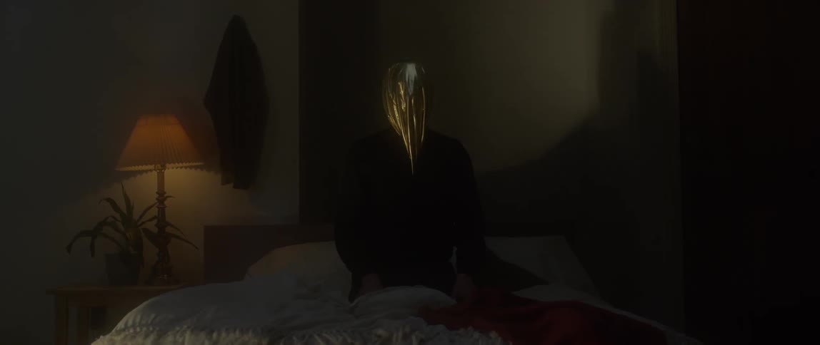 A woman wearing a gold face cover sits on a bed