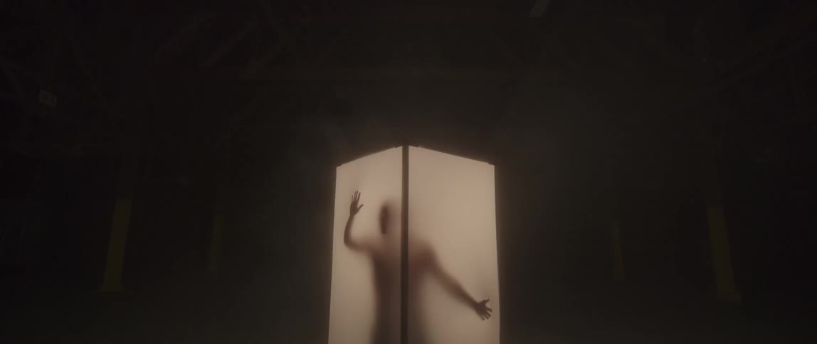 A silhouetted man stands in a glowing column and rubs his hands on the walls