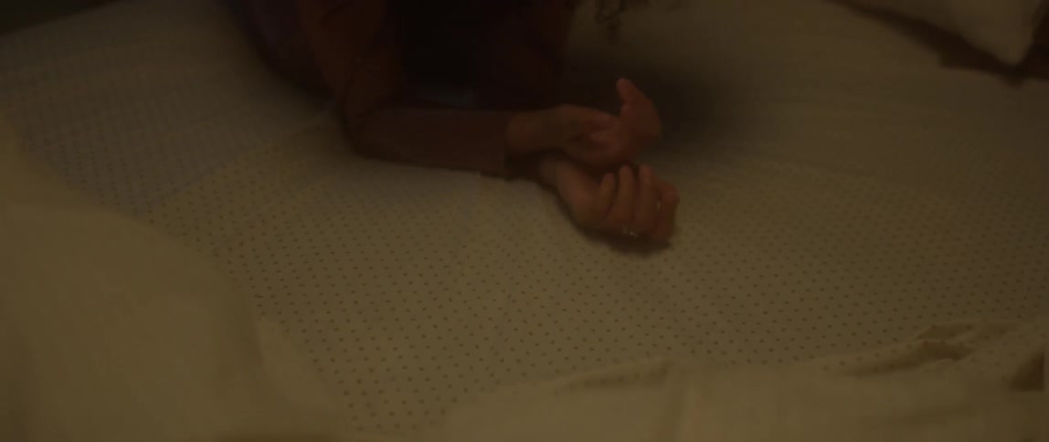A woman rubs her hands on sheets on a bed