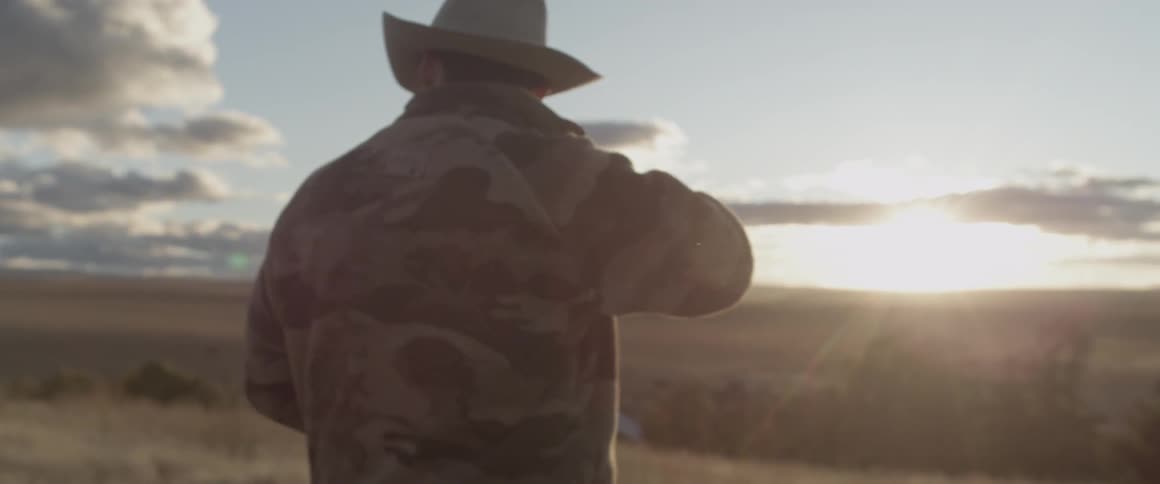 A man in a cowboy hat walks on a grassy hill