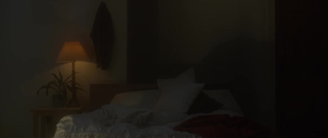 Pillows and sheets sit on a bed in a dark room