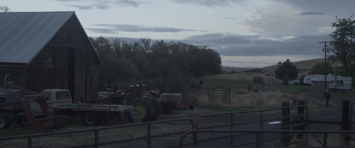 A truck and tractor are parked next to a barn on a rural farm