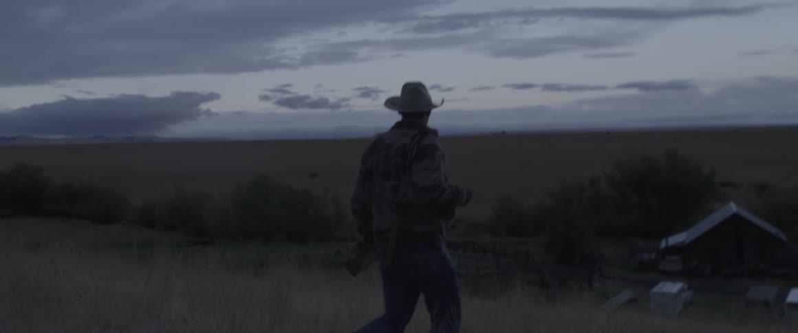 A man is walking across the pasture of a ranch