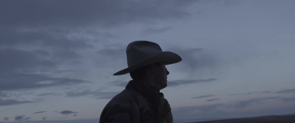 A man in a cowboy hat walks outside at dusk