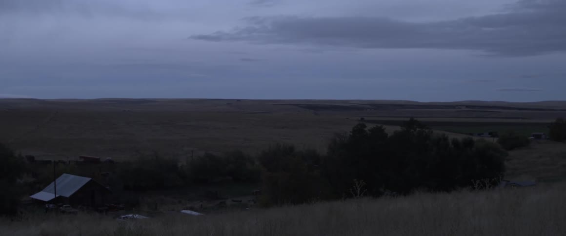 Fields and trees sit under a cloudy sky
