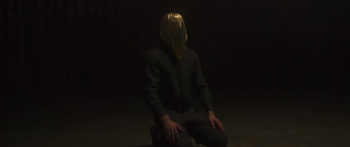 A man kneels on the ground while wearing a metallic bag over his head
