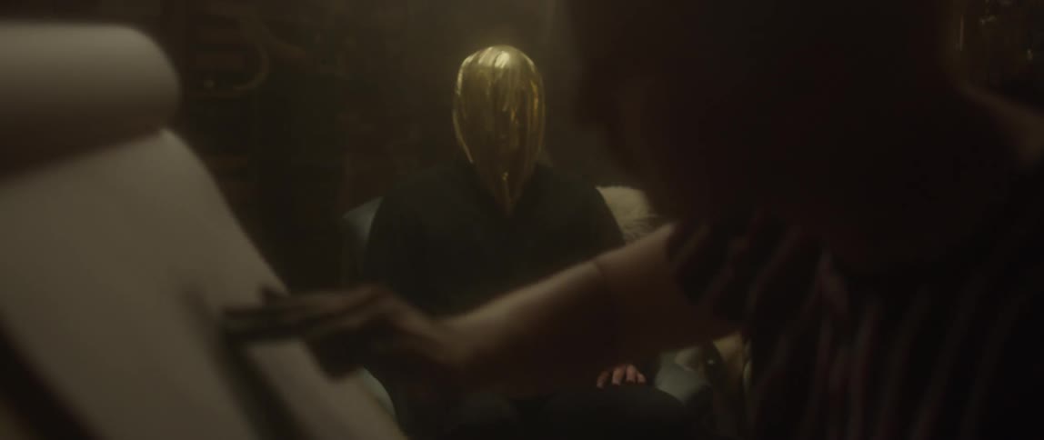 Person sketches on a piece of paper with a person sitting on the couch with their head covered