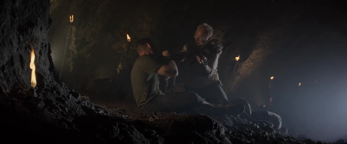 Two men play violins in a cave